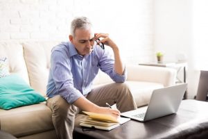 Man sits on couch while talking on the phone, learning about insurance benefits