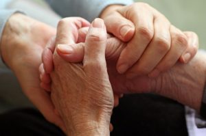 Younger person holding elderly person's hands in a comforting way
