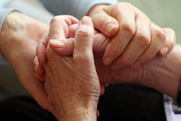 Younger person holding elderly person's hands in a comforting way