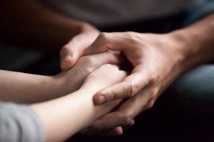 Focused on hands, man holding woman's hands in a comforting way