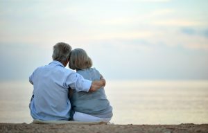 Older husband and wife sitting at beach, peacefully looking at the water