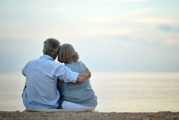 Older husband and wife sitting at beach, peacefully looking at the water