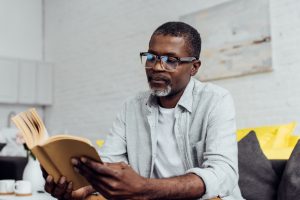 Middle-aged man wearing glasses sitting on couch, reading a book