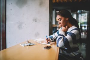 Young woman sitting at counter in coffee shop, journaling in notebook