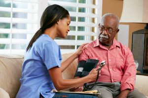 At home nurse taking blood pressure of older male patient, sitting on couch