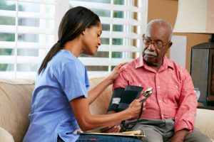 Female nurse taking elderly man's blood pressure at his home