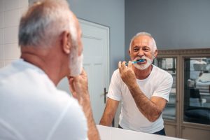 Older man looking into bathroom mirror while brushing his teeth