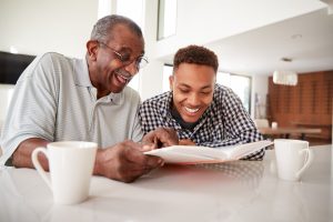 Grandfather and grandson sitting at kitchen table, looking at book together, laughing