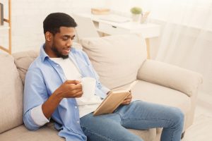 Man sitting on couch with mug and book