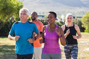 Group of 4 middle-aged adults running together through park