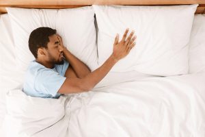 Young man lying bed, touching partner's pillow, missing her