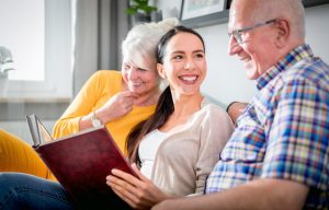 Young woman sitting with grandparents, looking at photo album and smiling