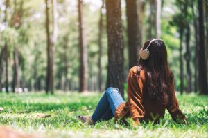 Woman sitting outside in the woods, trees and green grass, quite and contemplative