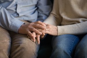 Man and woman sitting down, holding hands, focus on hands as they rest on laps