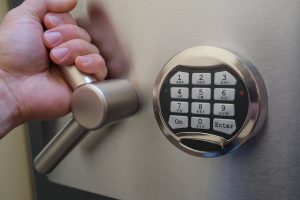 focus on front of a safe with number pad, hand on lever to open