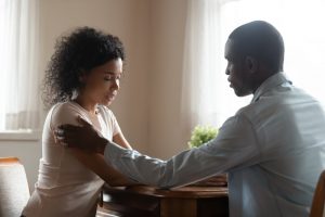 Husband comforting wife as they sit at table, hand on arm