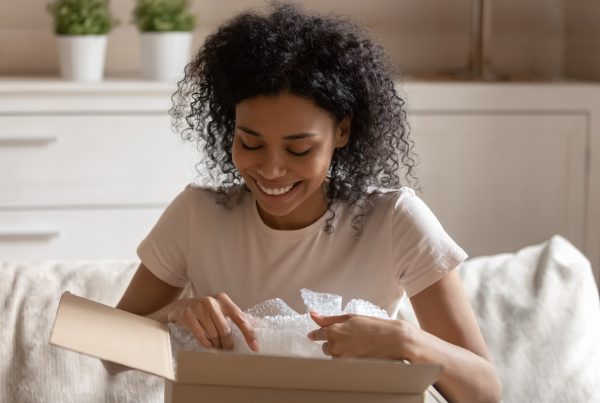 Young woman sitting on couch opening a box and smiling