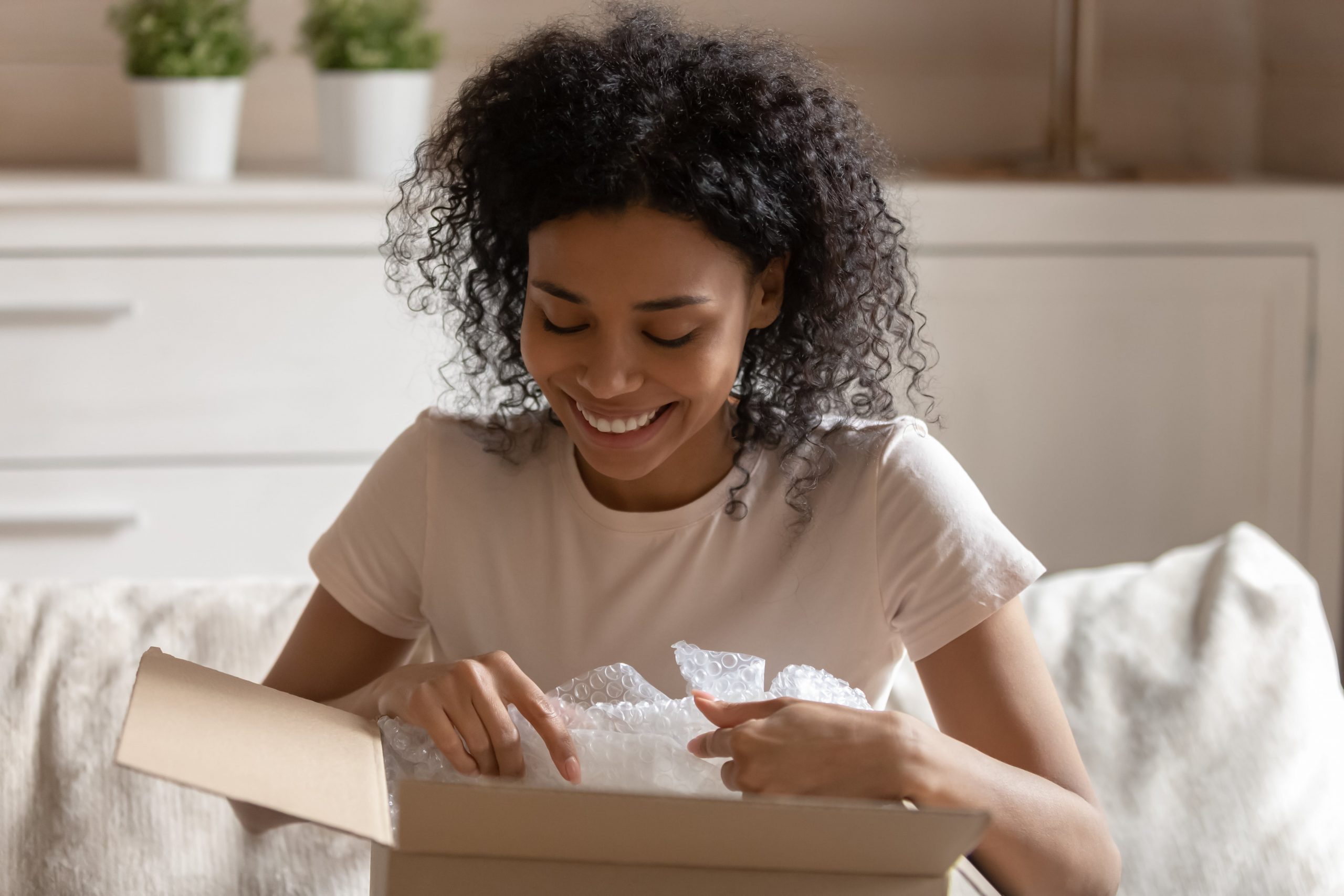 Young woman sitting on couch opening a box and smiling