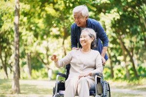 Older man pushing older woman in wheelchair, outside and smiling