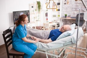 Nurse holding patient's hand, who is lying in a hospital bed in their home