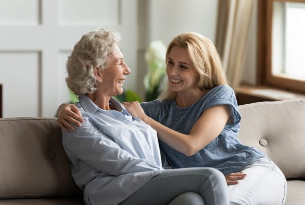 Mother and adult daughter sitting on couch talking and smiling