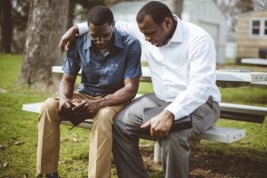 Two male friends sitting together, praying