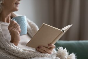 Woman sitting in chair, wrapped in a blanket with a open book and light blue mug