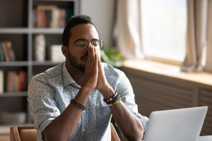 Man sitting at table with computer, eyes closed, breathing deeply