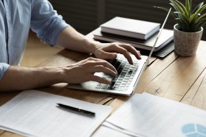 Man in blue shirt sitting at desk and typing on a computer