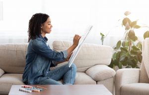 Woman sitting on couch as she draws on canvas, expressing herself