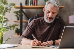 Man sitting at a desk at home, writing in a notebook