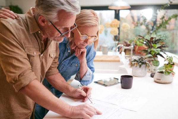 Older man and wife standing at kitchen counter looking over documents