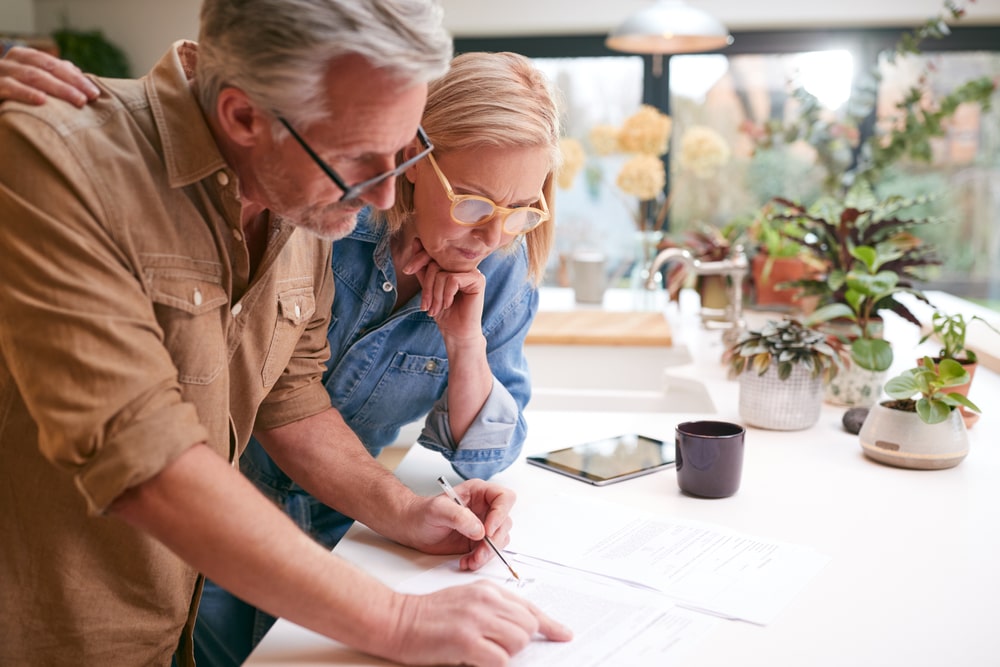 Older man and wife standing at kitchen counter looking over documents