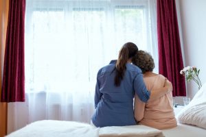 At home hospice nurse sitting with patient, giving a hug as they look out the window