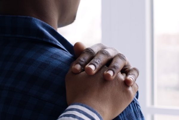 Man looking out window, friend places comforting hand on shoulder