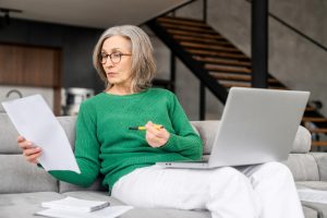 Woman sitting on couch with computer in lap, reading documents