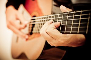 Man playing guitar, focus on strings and hands