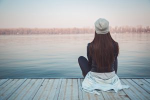 Woman sitting quietly on wooden pier, looking out at lake