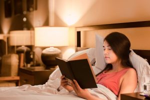 Woman sitting in bed reading a book with the lights low