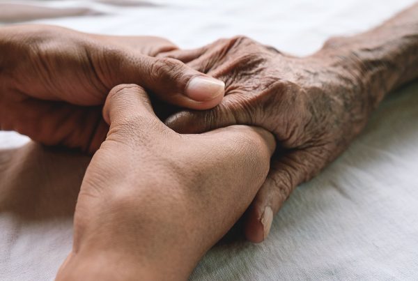 Focus on hands resting on bed, young person holding elderly person's hand