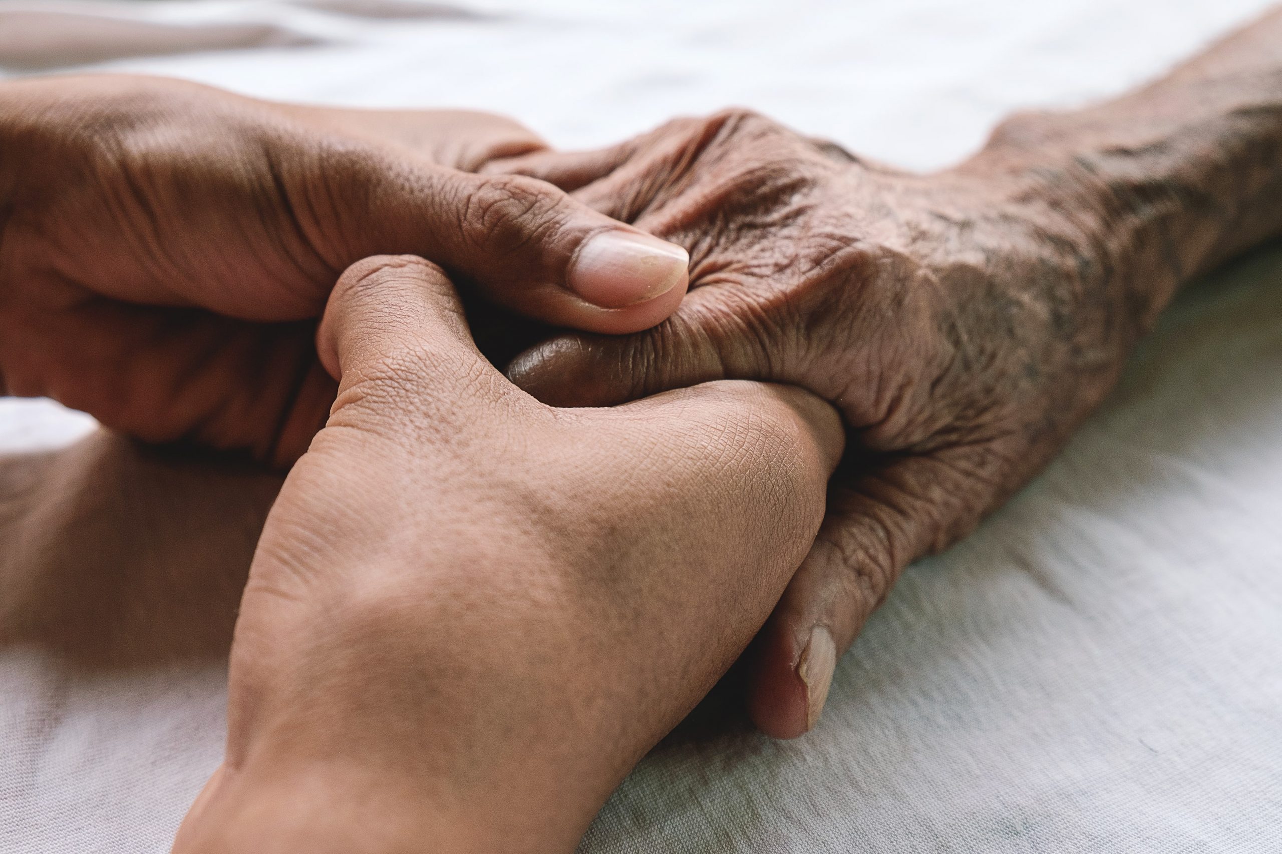 Focus on hands resting on bed, young person holding elderly person's hand