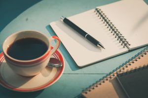 Open notebook with coffee and pen on blue table