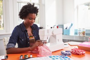 Woman sitting in sunroom at home, sewing on sewing machine