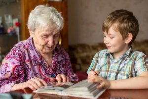 Great-grandmother sitting at table, looking at old photo album with grandson