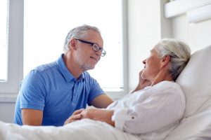 Husband talking to wife as she lies in hospital bed