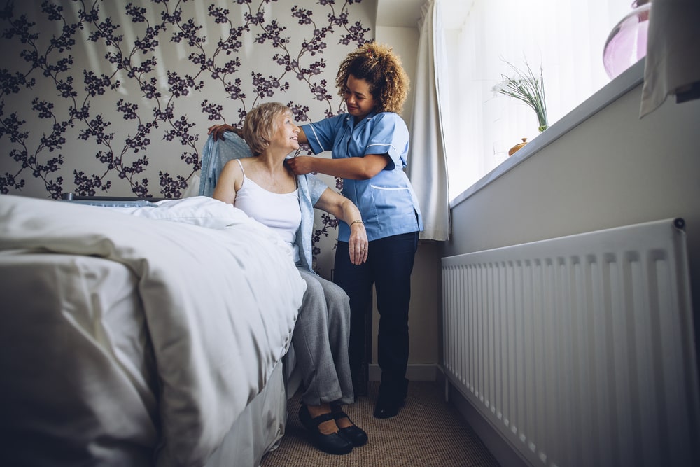 At home nurse helping female patient get out of bed, helping put on cardigan