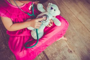 Little girl in pink dress playing doctor with stuffed bear