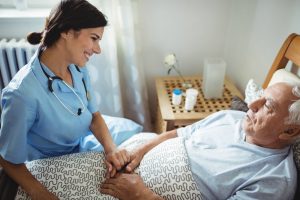 Nurse sitting at older mans' bedside, holding hand and smiling