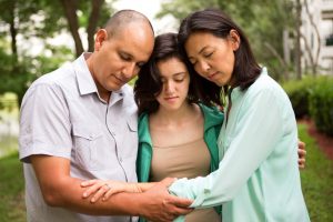 Mother, father, and teenage daughter praying together