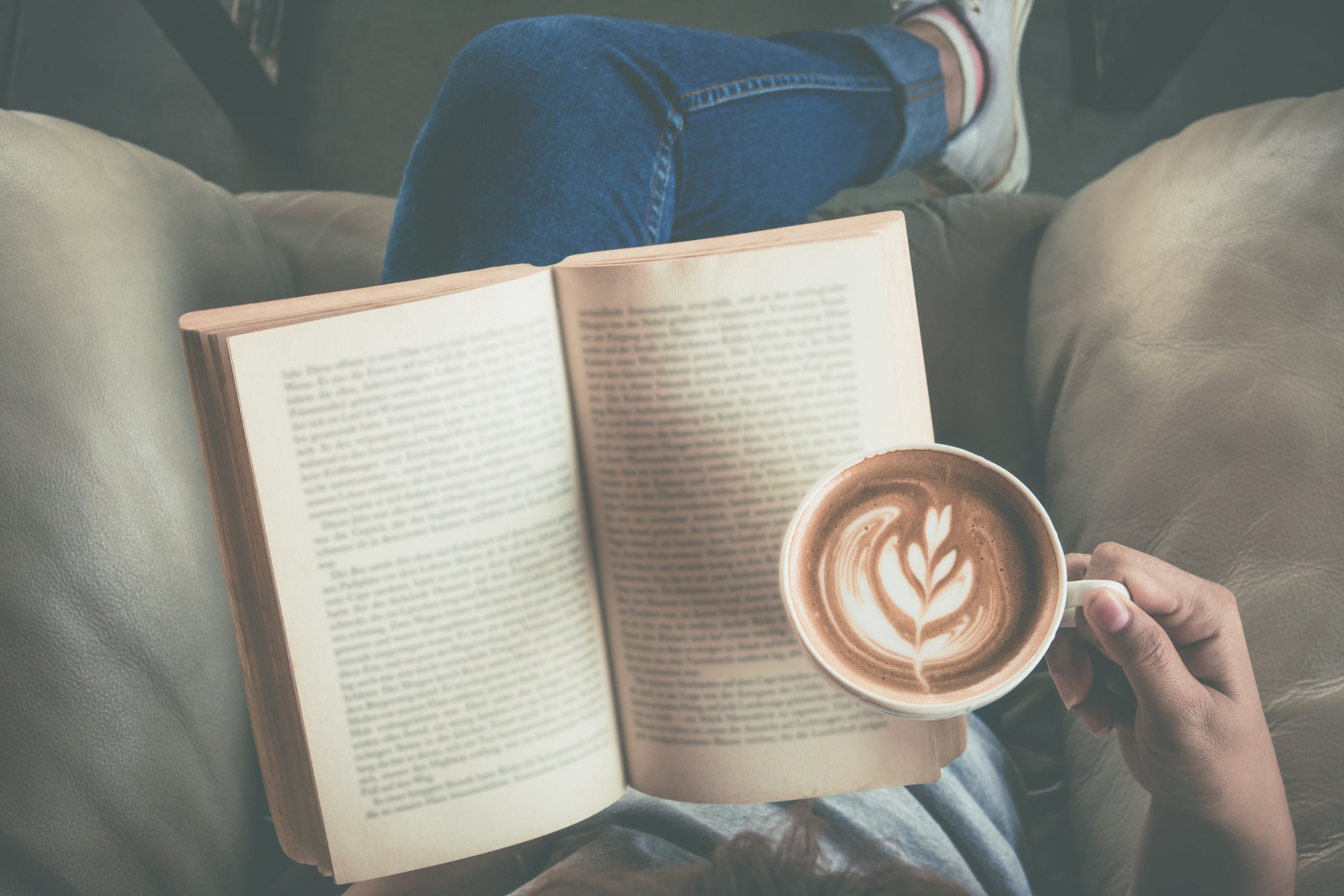 Person sitting on couch, reading and holding coffee